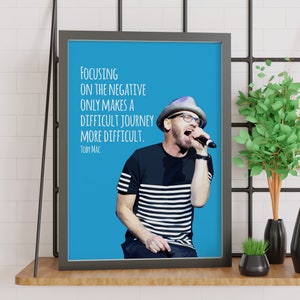 May include: A blue background with a quote by Toby Mac that reads "Focusing on the negative only makes a difficult journey more difficult."  A man with a striped shirt and a hat is singing into a microphone.