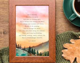 May include: A framed print with a watercolor painting of a forest scene at sunset. The print features a poem about life, with the text "Life is amazing. And then it's awful. And then it's amazing again." and the author's name "L.R. KNOST".