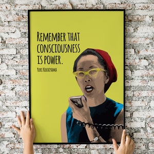 May include: A yellow poster with a black frame featuring a woman with a red headband and yellow glasses speaking into a microphone. The poster has the text "Remember that consciousness is power. Yuri Kochiyama."