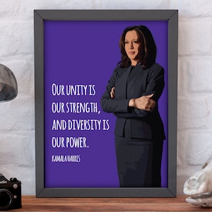 May include: A framed print with a purple background featuring a woman with her arms crossed. The quote "Our unity is our strength, and diversity is our power." is printed in white text below the woman. The woman's name, "Kamala Harris", is printed in white text below the quote.