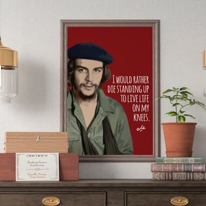 以下が含まれることがあります： 赤い背景に、緑のシャツと青いベレー帽をかぶった男性の肖像画が描かれた額縁付きポスター。肖像画の下には、「膝をつくよりも立って死ぬ方がましだ」という引用が白文字で書かれている。