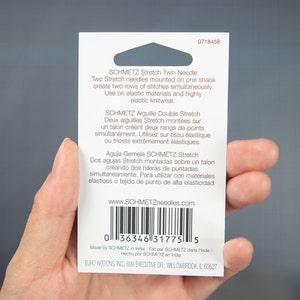 Peut inclure: Une carte blanche avec du texte noir d&eacute;crivant l'aiguille double extensible SCHMETZ et l'aiguille double extensible SCHMETZ. La carte comprend &eacute;galement un code-barres et l'adresse du site Web www.SCHMETZneedles.com.