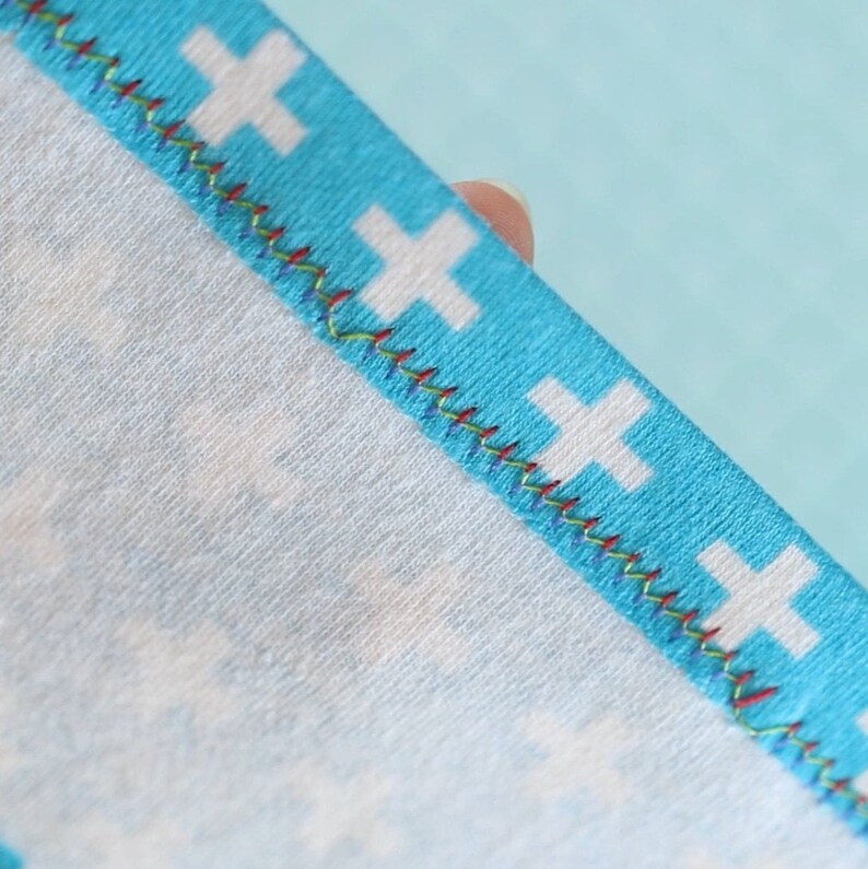 Peut inclure: Gros plan sur un tissu bleu avec un motif de croix blanches. Le tissu a une couture en zigzag color&eacute;e le long du bord.