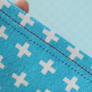 Peut inclure: Gros plan sur un tissu bleu avec un motif de croix blanches. Le tissu pr&eacute;sente deux rang&eacute;es de coutures, une rouge et une bleue.