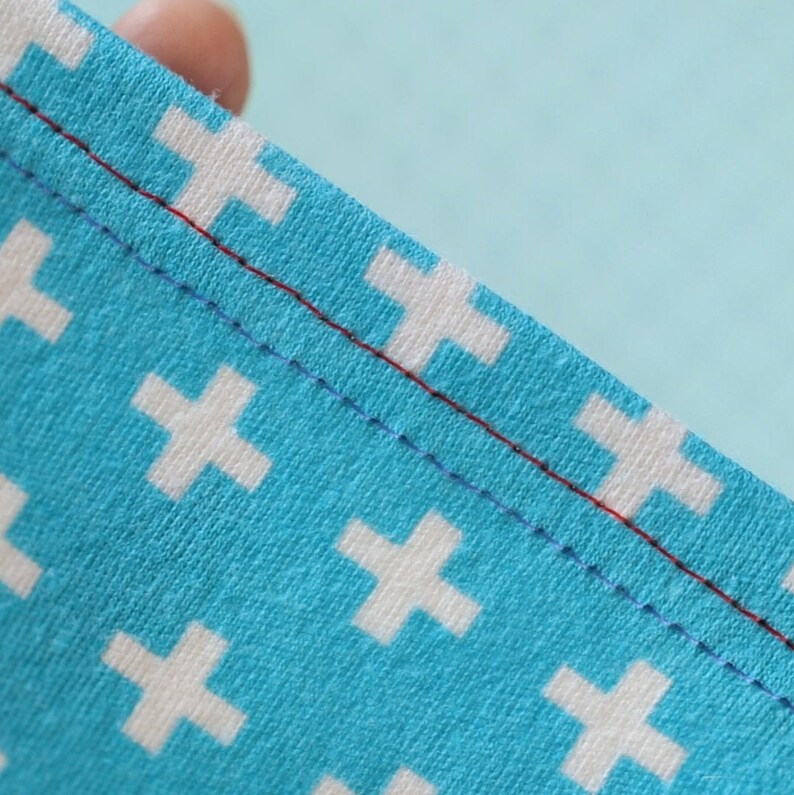 Peut inclure: Gros plan sur un tissu bleu avec un motif de croix blanches. Le tissu pr&eacute;sente deux rang&eacute;es de coutures, une rouge et une bleue.