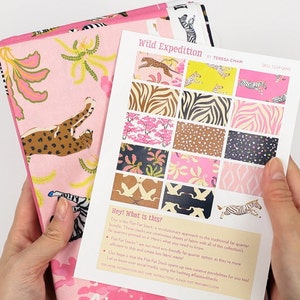 May include: A sheet of fabric with a pink background and a variety of animal prints, including zebras, leopards, and birds. The fabric is part of a collection called "Wild Expedition" by Teresa Chan. The sheet is folded in half and held by a person's hands.