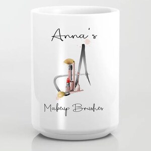 May include: White ceramic mug with the text "Anna's Makeup Brushes" and a black and white illustration of the letter "A" with makeup brushes and lipstick inside.