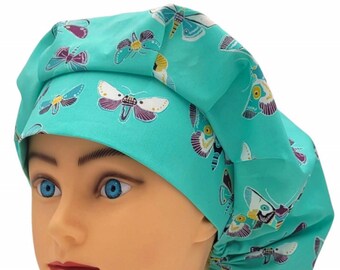 May include: A teal scrub cap featuring a repeating pattern of moths in shades of white, purple, and yellow. The cap has a wide, structured front band and a gathered, voluminous back section designed to provide a secure and comfortable fit.