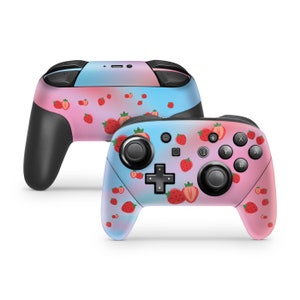 May include: A pink and blue Nintendo Switch controller with a strawberry pattern. The controller has a pink and blue ombre design with white strawberries scattered across the surface.