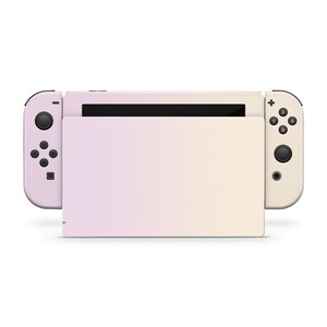 May include: A pink and cream Nintendo Switch console with a gradient design. The console is closed and the Joy-Con controllers are attached.