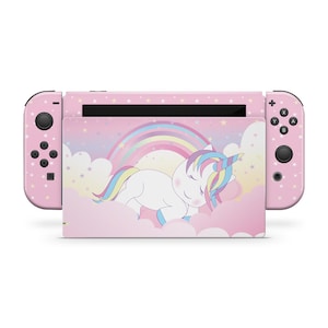 May include: A pink Nintendo Switch console with a unicorn theme. The console and controllers are covered in a pink pattern with white stars. The center screen features a sleeping unicorn with a rainbow and clouds.