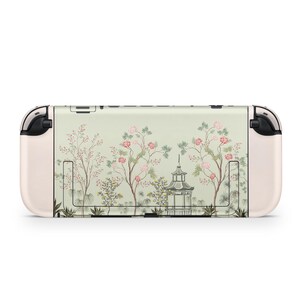 May include: A Nintendo Switch console with a custom skin featuring a serene Asian garden design. The skin showcases a light green background with illustrations of trees, flowers, and a pagoda. The console has a cream-colored body and black accents.