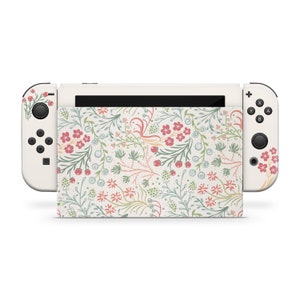 May include: A white Nintendo Switch console with a floral pattern skin. The skin features a delicate design of pink and green flowers and leaves on a cream background.
