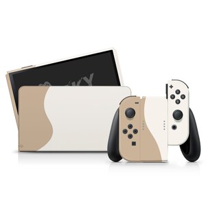 May include: A beige and white Nintendo Switch console with two matching controllers. The console has a curved design and the controllers have black buttons.
