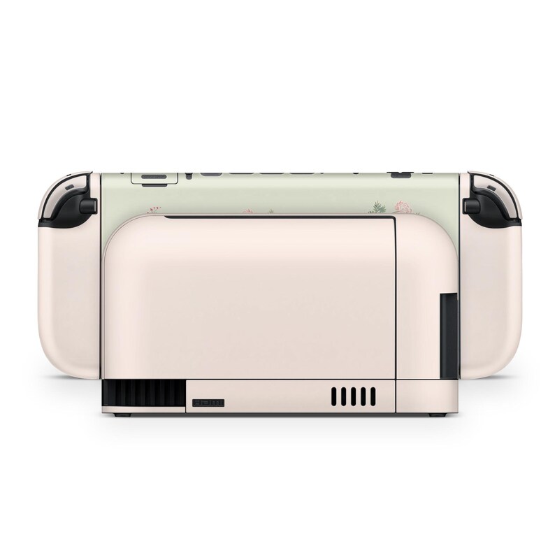 May include: A blush pink and white Nintendo Switch console. The console features a floral pattern on the top and sides. The design includes a light green background with pink flowers. The console has black accents.