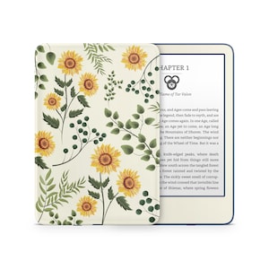 May include: A cream-colored e-reader with a floral sunflower design cover. The cover features yellow sunflowers, green leaves, and stems. The e-reader is open, displaying text from "Flame of Tar Valon" in a serif font.