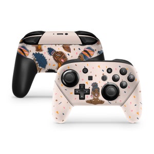May include: Two wireless game controllers with a custom skin featuring illustrations of women with colorful head wraps and hairstyles. The controllers have black buttons and joysticks, and a light beige background with confetti.