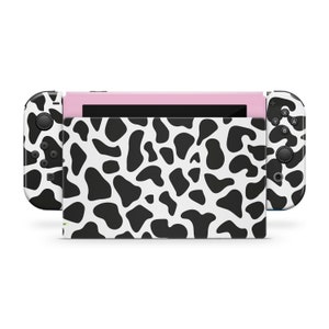 May include: A black and white cow print skin for a Nintendo Switch console. The skin covers the console, the joy-cons, and the screen.