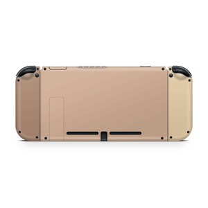 Pu&ograve; includere: Una console Nintendo Switch beige con pulsanti neri e un bordo dorato. La console &egrave; mostrata frontalmente.