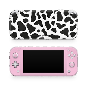 May include: A pink Nintendo Switch Lite console with a black and white cow print skin. The console has a black screen and white buttons.