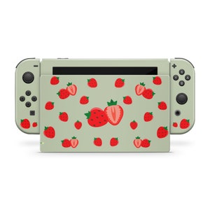 May include: A green Nintendo Switch console with a custom skin featuring a pattern of red strawberries. The console is closed and the Joy-Con controllers are attached.