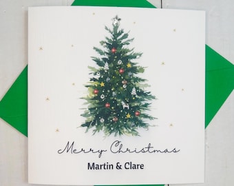 May include: A white Christmas card featuring a watercolour illustration of a green Christmas tree adorned with baubles and a silver star on top. The text "Merry Christmas Martin & Clare" is printed beneath the tree.