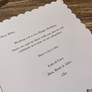 May include: A white card with a scalloped edge and a handwritten message wishing someone a happy birthday. The message says "Dear Elise, Wishing you a very Happy Birthday. Sorry we can't be there with you, but we will celebrate next time we are altogether. Have a lovely day Lots of Love Ben, Rosie & Alice XXX"