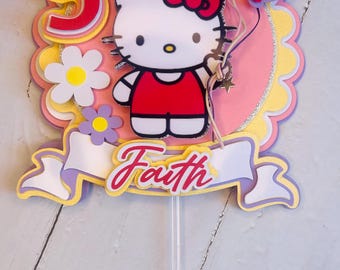 May include: A pink and yellow Hello Kitty cake topper with a red number 5, a white banner with the name "Faith" and balloons.