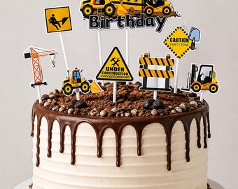 May include: A round cake with white frosting and dark chocolate ganache drips, topped with construction-themed paper decorations including a Happy Birthday sign, a crane, a forklift, and yellow warning signs with text like Under Construction.