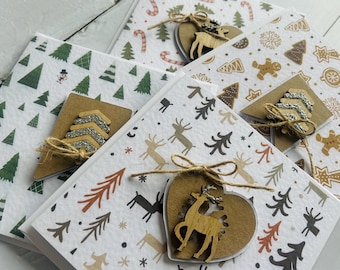 May include: A selection of Christmas greeting cards with festive designs. The cards display patterns of trees, reindeer, and gingerbread men. Each card is decorated with a wooden embellishment and tied with twine.