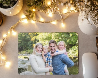 May include: Rectangular mousepad displaying a family portrait set in a natural environment. The image shows a smiling family of four, with a woman, a man, and two young children. The mousepad is surrounded by fairy lights and a white computer mouse.