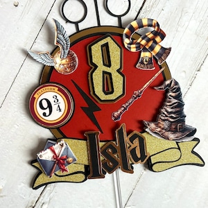 May include: A red and gold cake topper featuring a number 8, a lightning bolt, a wand, a hat, a scarf, a golden snitch, and the text "Platform 9 3/4". The topper also includes a banner with the name "Isla" in gold letters.