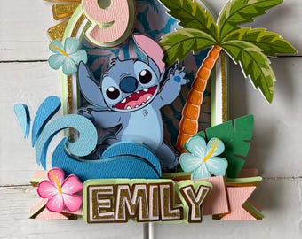 May include: A vibrant cake topper featuring the character Stitch. The design includes the number 9, a palm tree, and the name "EMILY". The topper is decorated with pink, blue, green, and gold accents, suitable for a birthday celebration.