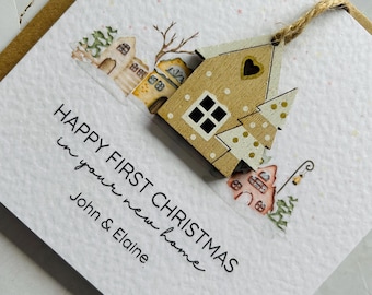 May include: A Christmas card with a wooden house ornament and the text "HAPPY FIRST CHRISTMAS in your new home" with the names "John & Elaine". The card features watercolor illustrations of houses and trees.
