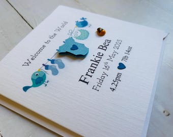 May include: A baby announcement card with the text "Welcome to the World." The card features a blue bird, baby clothes, and the name "Frankie Bea," along with the birth date, time, and weight: 7lb 14oz.