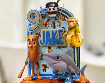 May include: A vibrant cake topper with the name "Jake" and the number "9". The topper showcases cartoon characters such as a ninja, monkey, and shark. The cake is decorated with brown frosting.
