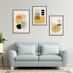 Può includere: Tre stampe d'arte astratta in cornici nere sono appese a una parete bianca sopra un divano blu chiaro con due cuscini di colore verde chiaro. Le stampe presentano forme geometriche in tonalità di giallo, verde, rosa e nero.