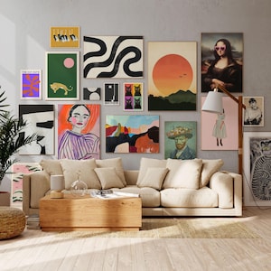 Op de afbeelding: Een woonkamer met een beige bank, een houten salontafel en een galerijmuur met ingelijste kunstdrukken. De kunstwerken omvatten abstracte ontwerpen, portretten en landschappen, met een verscheidenheid aan kleuren en stijlen. Een grote plant in pot en een geweven poef dragen bij aan de inrichting.