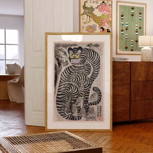 Peut inclure: Une estampe encadr&eacute;e en noir et blanc d'un tigre avec un &oelig;il jaune. Le tigre est assis sur ses haunches, la queue enroul&eacute;e autour de son corps. L'estampe est entour&eacute;e d'un fin cadre dor&eacute;. L'estampe est accroch&eacute;e &agrave; un mur blanc.