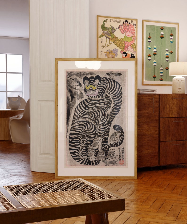 Peut inclure: Une estampe encadr&eacute;e en noir et blanc d'un tigre avec un &oelig;il jaune. Le tigre est assis sur ses haunches, la queue enroul&eacute;e autour de son corps. L'estampe est entour&eacute;e d'un fin cadre dor&eacute;. L'estampe est accroch&eacute;e &agrave; un mur blanc.