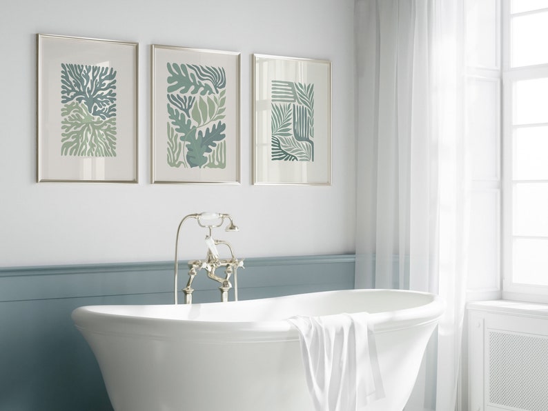 K&ouml;nnte beinhalten: Drei gerahmte botanische Kunstdrucke in Gr&uuml;n- und Blaut&ouml;nen h&auml;ngen &uuml;ber einer wei&szlig;en Badewanne. Die Drucke zeigen abstrakte Blatt- und Pflanzendesigns. Das Badezimmer hat eine klassische, spa-&auml;hnliche &Auml;sthetik mit einer wei&szlig;en Wanne und einer blauen Akzentwand.