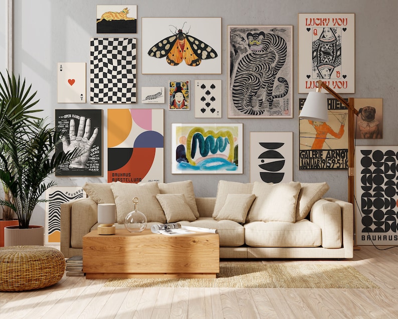 Op de afbeelding: Een woonkamer interieur met een beige bank, een houten salontafel en een vloerkleed. De muur is versierd met een galerijmuur van verschillende prints, waaronder een zwart-wit geruit patroon, een tijgerprint, een geometrisch patroon en een handafdruk. Er is een staande lamp met een witte kap en een kamerplant in de hoek.