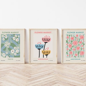 May include: Three framed prints with a floral theme. Each print features a different floral design and the city name: Tokyo, Stockholm, and Amsterdam. The prints have a light beige background and the text "Flower Market" is at the top of each print.