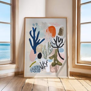 Può includere: Stampa d'arte astratta in una cornice di legno. L'opera presenta forme e forme colorate, tra cui strutture simili a coralli in blu, nero e verde, insieme a forme circolari rosa e arancioni. Lo sfondo è beige neutro.
