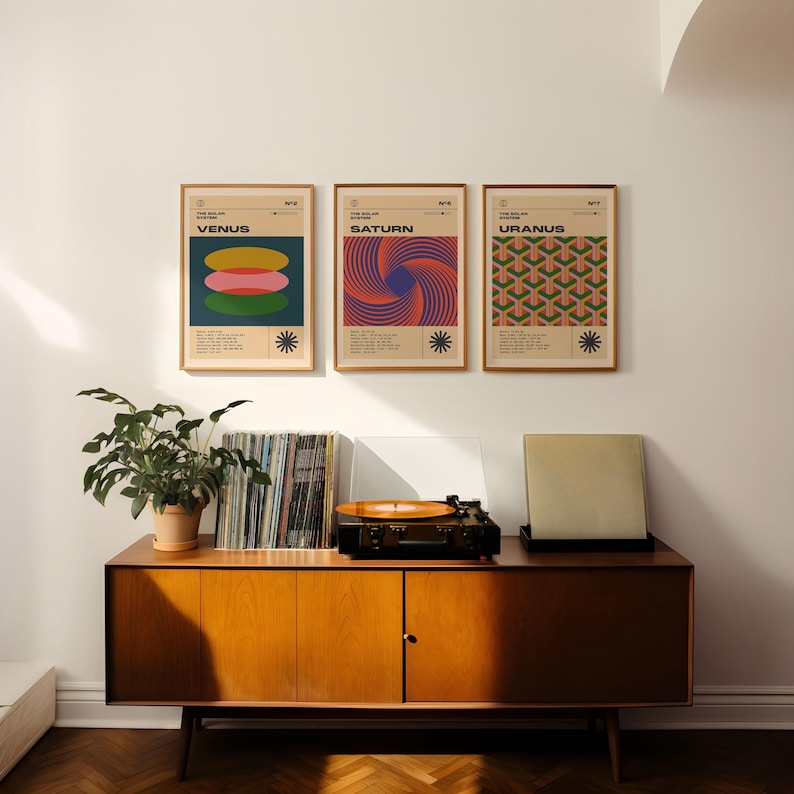 May include: Three framed posters with mid-century modern designs of planets Venus, Saturn, and Uranus hang above a wooden cabinet. A record player and vinyl records sit on the cabinet, with a potted plant to the left.
