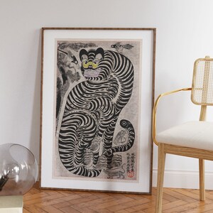 Peut inclure: Une illustration en noir et blanc d'un tigre aux yeux jaunes. Le tigre est assis sur ses haunches, la queue enroul&eacute;e autour de son corps. L'illustration est encadr&eacute;e dans un cadre en bois brun.