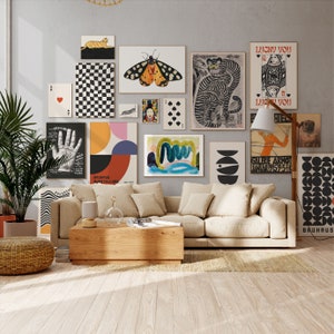 Op de afbeelding: Een woonkamer interieur met een beige bank, een houten salontafel en een verscheidenheid aan kleurrijke wandkunst, waaronder een vlinder, een geometrisch ontwerp en een handafdruk. De wandkunst hangt aan een grijze muur.