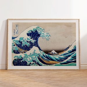 May include: A wood-framed print of a Japanese woodblock print depicting a large wave crashing over a boat with Mount Fuji in the background. The wave is blue and white with splashes of green and the sky is a light gray.