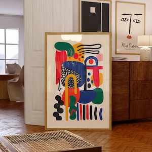 Puede incluir: Impresión de arte abstracto con un diseño colorido que presenta formas rojas, amarillas, azules, verdes y negras. La impresión está enmarcada en un marco dorado y cuelga de una pared.