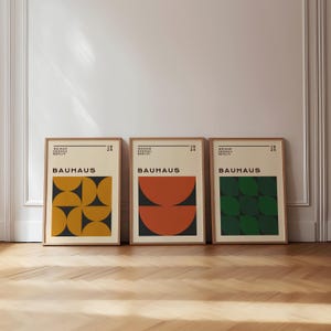 May include: Three framed Bauhaus art prints. Each print features a geometric design in shades of yellow, orange, and green against a cream background. The word "BAUHAUS" is prominently displayed on each print.
